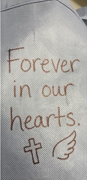 A CliniCareBag with the words "Forever in our hearts" and a cross and angel wing